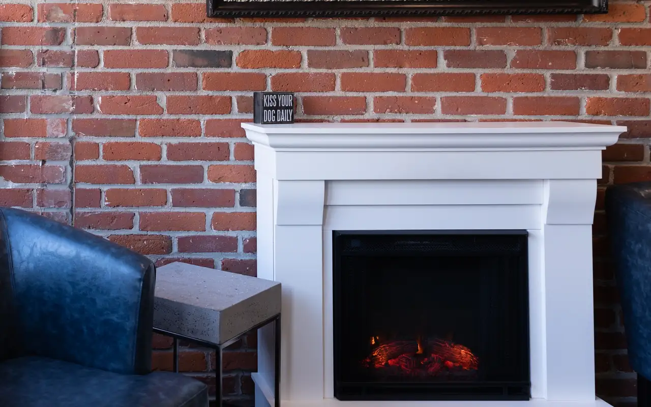 The front lobby at Vultaggio Dental in Concord: a brick wall, a white fireplace, a framed antique map and a leather armchair.